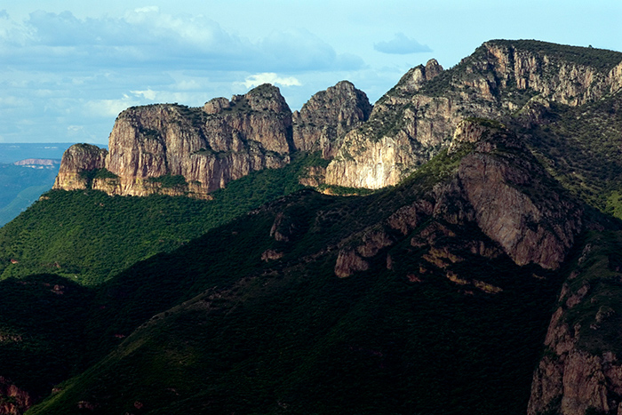 Fotografía de una barranca donde se aprecia el color verde de las montañas y al fondo el horizonte con nubres blancas.